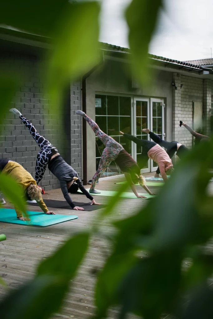 Cours de yoga collectif en extérieur, plusieurs pratiquantes en posture du chien tête en bas sur une terrasse en bois